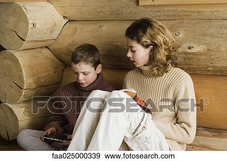 Teen girl and preteen boy sitting side by side, reading and playing video game View Large Photo Image Stock Photo - Teen girl and preteen boy sitting side by side, reading and playing video game. Fotosearch