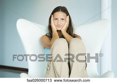 Teen girl sitting in arm chair, holding head in hands, looking at camera, three quarter length View Large Photo Image Stock Image - Teen girl sitting in arm chair, holding head in hands, looking at camera, three quarter length. Fotosearch