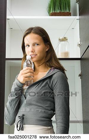 Teen girl standing by pantry, holding bottle of water View Large Photo Image Stock Photo - Teen girl standing by pantry, holding bottle of water. Fotosearch