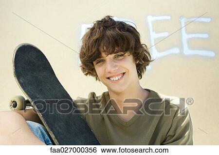 Teenage boy holding skateboard, smiling at camera, portrait View Large Photo Image Stock Photograph - Teenage boy holding skateboard, smiling at camera, portrait. Fotosearch