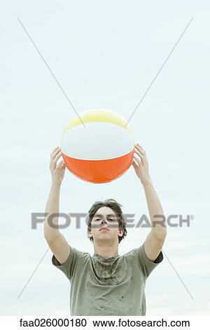 Teenage boy holding up beach ball, looking at camera View Large Photo Image Stock Image - Teenage boy holding up beach ball, looking at camera. Fotosearch