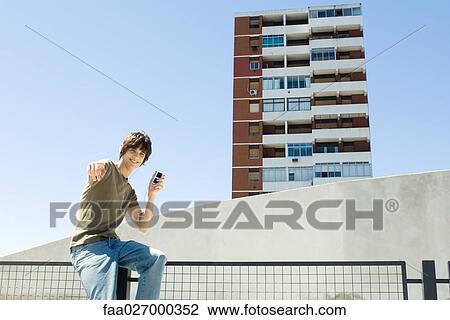 Teenage boy sitting outdoors, listening to mp3 player, pointing at camera View Large Photo Image Stock Image - Teenage boy sitting outdoors, listening to mp3 player, pointing at camera. Fotosearch