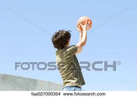 Teenage boy standing outdoors, throwing basketball, low angle view View Large Photo Image Picture - Teenage boy standing outdoors, throwing basketball, low angle view. Fotosearch