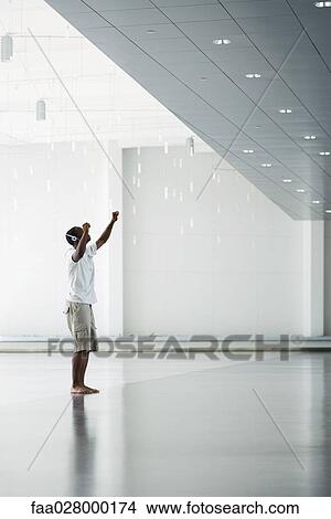 Teenage boy standing with arms raised, listening to headphones, side view View Large Photo Image Picture - Teenage boy standing with arms raised, listening to headphones, side view. Fotosearch