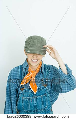 Stock Photo - Teenage girl dressed in overalls, hat covering eyes, smiling. Fotosearch