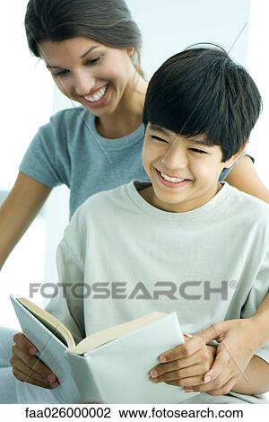 Stock Image - Teenage girl helping boy read book. Fotosearch