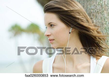 Teenage girl listening to earphones outdoors, hair tousled by breeze, looking away View Large Photo Image Stock Image - Teenage girl listening to earphones outdoors, hair tousled by breeze, looking away. Fotosearch