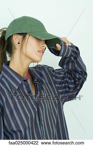 Stock Image - Teenage girl pulling cap down over her eyes. Fotosearch
