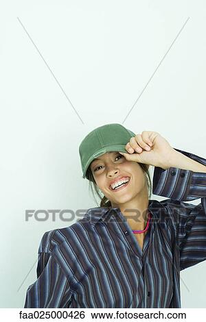 Teenage girl putting on cap, smiling at camera View Large Photo Image Stock Photograph - Teenage girl putting on cap, smiling at camera. Fotosearch