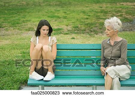 Teenage girl sitting apart from grandmother on bench, both frowning View Large Photo Image Stock Image - Teenage girl sitting apart from grandmother on bench, both frowning. Fotosearch