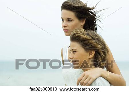 Stock Image - Teenage girl standing with arm around brother's shoulder, both looking at view. Fotosearch