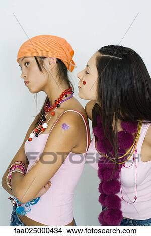 Teenage girl standing with arms folded, friend standing behind and looking over her shoulder View Large Photo Image Picture - Teenage girl standing with arms folded, friend standing behind and looking over her shoulder. Fotosearch