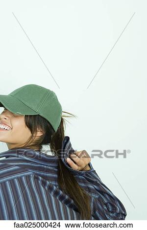 Teenage girl wearing baseball cap, looking over shoulder, cropped view View Large Photo Image Picture - Teenage girl wearing baseball cap, looking over shoulder, cropped view. Fotosearch
