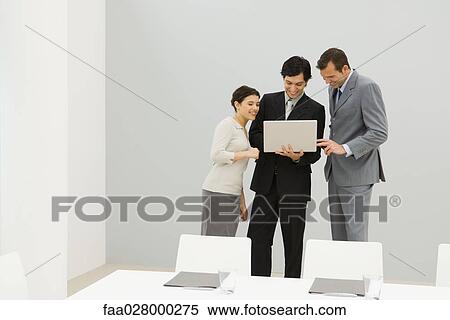 Three business associates standing in conference room, looking at laptop computer together View Large Photo Image Stock Photography - Three business associates standing in conference room, looking at laptop computer together. Fotosearch