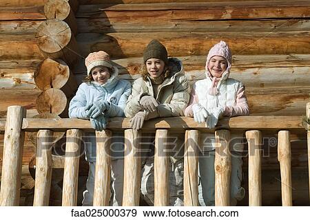 Stock Photo - Three preteen or teen girls standing on deck of log cabin, looking away, low angle view. Fotosearch