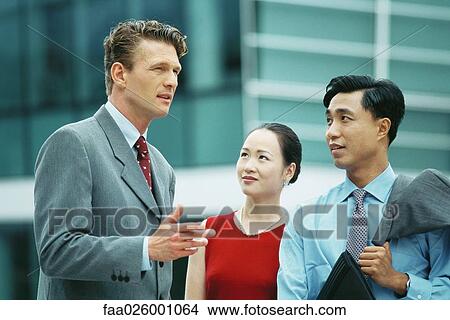 Three professionals chatting outdoors, one gesturing with hand View Large Photo Image Picture - Three professionals chatting outdoors, one gesturing with hand. Fotosearch