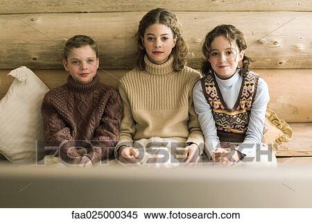 Stock Photography - Three young siblings watching TV and eating marshmallows. Fotosearch
