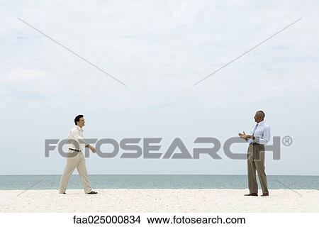 Two businessman walking toward each other on the beach, both smiling View Large Photo Image Picture - Two businessman walking toward each other on the beach, both smiling. Fotosearch