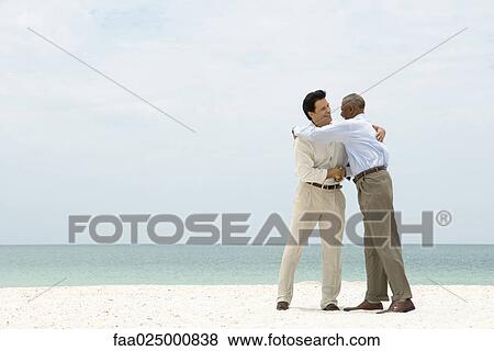 Two businessmen shaking hands and embracing on the beach View Large Photo Image Stock Photo - Two businessmen shaking hands and embracing on the beach. Fotosearch