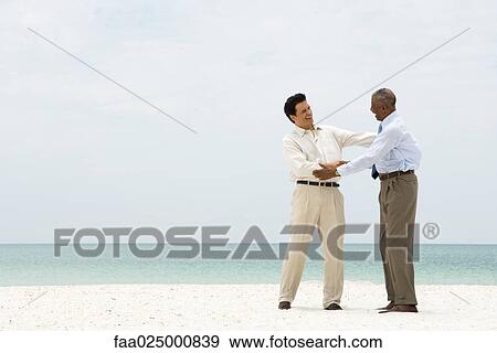 Two businessmen shaking hands on the beach, smiling at each other View Large Photo Image Stock Photo - Two businessmen shaking hands on the beach, smiling at each other. Fotosearch