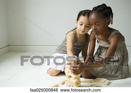 Two girls crouching, building tower with blocks together View Large Photo Image Stock Photo - Two girls crouching, building tower with blocks together. Fotosearch
