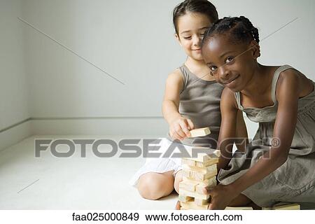 Two girls crouching, building tower with blocks together, one smiling at camera View Large Photo Image Stock Photo - Two girls crouching, building tower with blocks together, one smiling at camera. Fotosearch