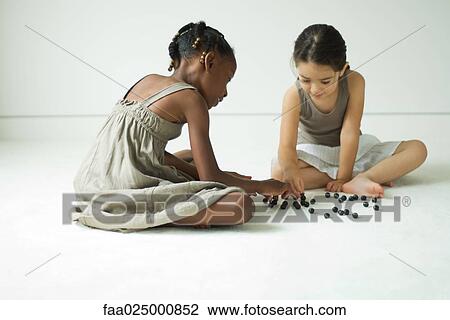 Two girls sitting on the ground playing with marbles View Large Photo Image Stock Image - Two girls sitting on the ground playing with marbles. Fotosearch