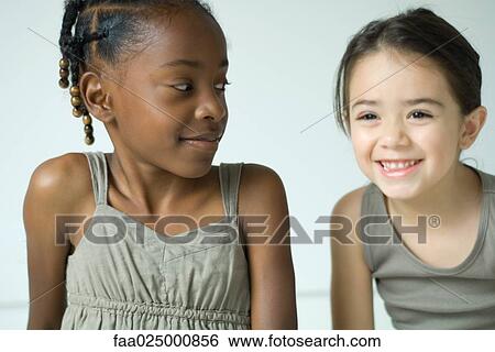 Two girls smiling, side by side, one looking at the other View Large Photo Image Stock Photograph - Two girls smiling, side by side, one looking at the other. Fotosearch