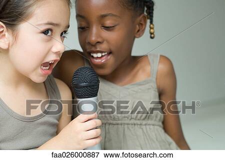 Two little girls singing into microphone together, close-up View Large Photo Image Stock Photo - Two little girls singing into microphone together, close-up. Fotosearch