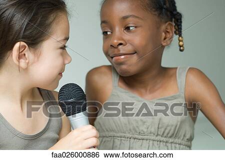 Stock Photograph - Two little girls smiling at each other, one holding microphone, close-up. Fotosearch