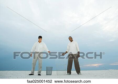 Two men at the beach holding their hands over garbage cans, one looking at camera View Large Photo Image Stock Image - Two men at the beach holding their hands over garbage cans, one looking at camera. Fotosearch
