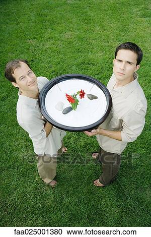 Two men holding up rock garden, one smiling, the other frowning, high angle view View Large Photo Image Stock Image - Two men holding up rock garden, one smiling, the other frowning, high angle view. Fotosearch