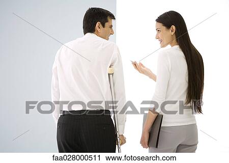 Stock Image - Two office colleagues talking, one using crutches. Fotosearch
