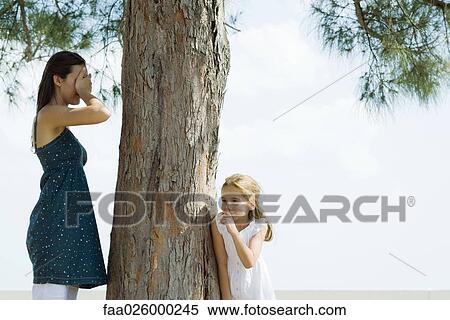 Two sisters playing hide-and-seek, one covering eyes with hands, the other peeking around tree trunk View Large Photo Image Stock Photography - Two sisters playing hide-and-seek, one covering eyes with hands, the other peeking around tree trunk. Fotosearch