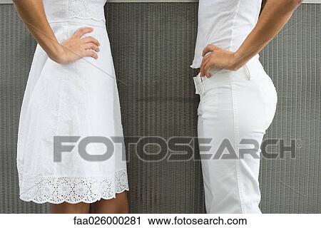 Stock Image - Two teenage girls standing face to face with hands on hips, cropped side view. Fotosearch