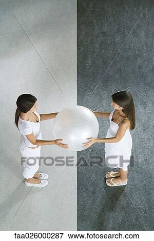 Two teenage girls standing face to face, holding fitness ball together, viewed from directly above View Large Photo Image Stock Photo - Two teenage girls standing face to face, holding fitness ball together, viewed from directly above. Fotosearch