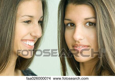 Picture - Two twin teenage sisters smiling, one looking at camera. Fotosearch