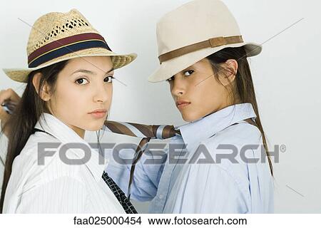 Two young female friends face to face, both wearing hats and ties, looking at camera View Large Photo Image Picture - Two young female friends face to face, both wearing hats and ties, looking at camera. Fotosearch