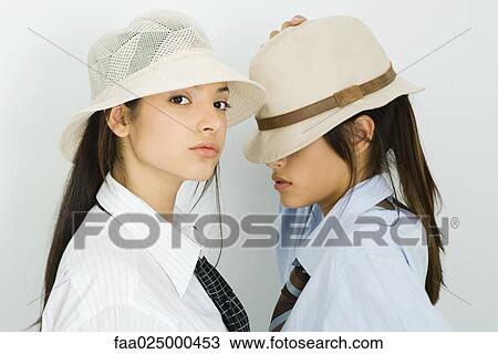 Two young female friends wearing hats, one looking at camera, the other's eyes covered View Large Photo Image Stock Image - Two young female friends wearing hats, one looking at camera, the other's eyes covered. Fotosearch