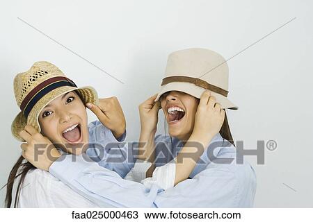 Two young friends pulling hats over each other's faces and smiling, one looking at camera View Large Photo Image Stock Image - Two young friends pulling hats over each other's faces and smiling, one looking at camera. Fotosearch