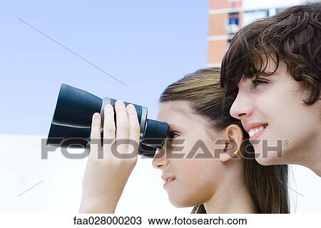Two young friends standing side by side outdoors, girl looking through binoculars, side view View Large Photo Image Stock Image - Two young friends standing side by side outdoors, girl looking through binoculars, side view. Fotosearch