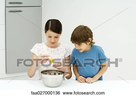 Two young siblings cooking together, girl cracking egg, both looking down View Large Photo Image Stock Photograph - Two young siblings cooking together, girl cracking egg, both looking down. Fotosearch