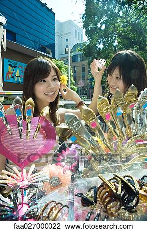 Two young women in street market, trying on hair accessories, smiling View Large Photo Image Stock Image - Two young women in street market, trying on hair accessories, smiling. Fotosearch