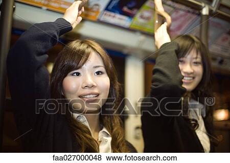 Two young women standing on subway, arms raised, smiling View Large Photo Image Stock Photo - Two young women standing on subway, arms raised, smiling. Fotosearch