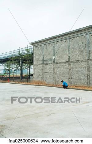 Urban scene, person crouching next to edge of building View Large Photo Image Picture - Urban scene, person crouching next to edge of building. Fotosearch