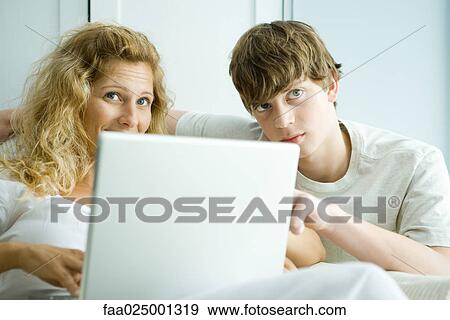 Stock Photo - Woman and teen son using laptop, looking up. Fotosearch