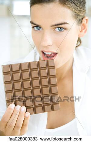Woman biting into large chocolate bar, looking at camera View Large Photo Image Stock Image - Woman biting into large chocolate bar, looking at camera. Fotosearch