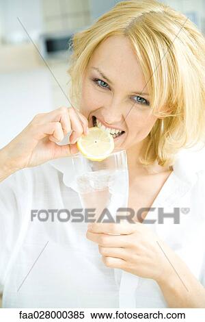 Woman holding glass of water, biting into lemon slice, looking at camera View Large Photo Image Stock Photography - Woman holding glass of water, biting into lemon slice, looking at camera. Fotosearch