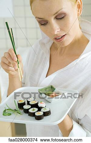 Woman holding maki sushi and chopsticks, looking down View Large Photo Image Picture - Woman holding maki sushi and chopsticks, looking down. Fotosearch