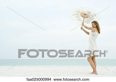Woman holding parasol on beach, full length View Large Photo Image Picture - Woman holding parasol on beach, full length. Fotosearch
